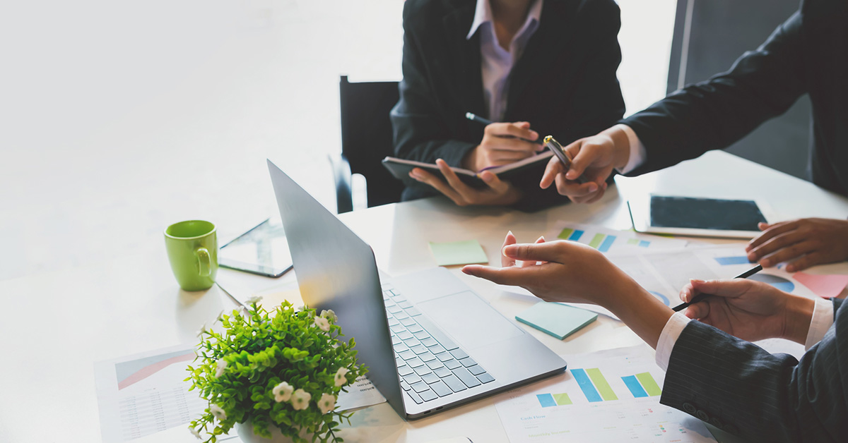 Three office workers discuss operations while overlooking data on a laptop.