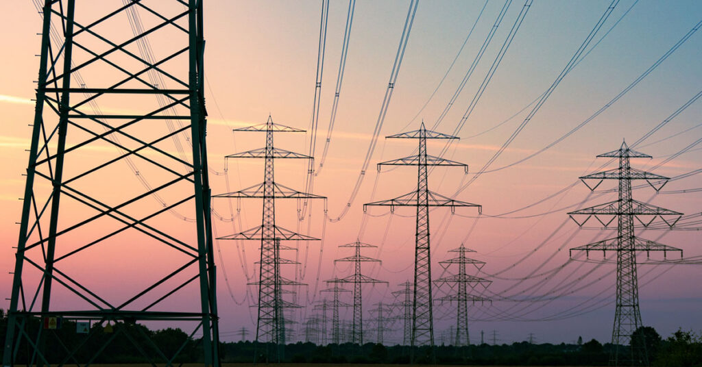 Power lines in a field at dusk with a sunset in the background