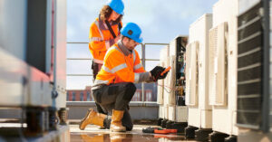 Two technicians perform repairs on an air conditioning unit.