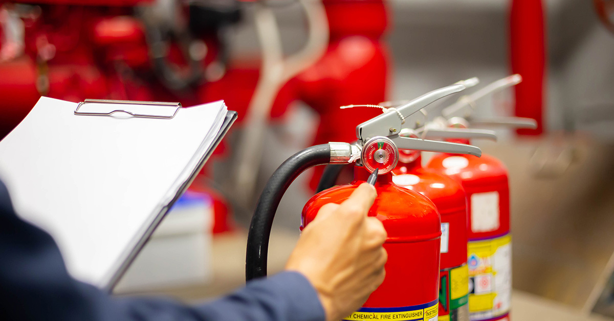 A worker performs an inspection on a set of fire extinguishers in a warehouse.