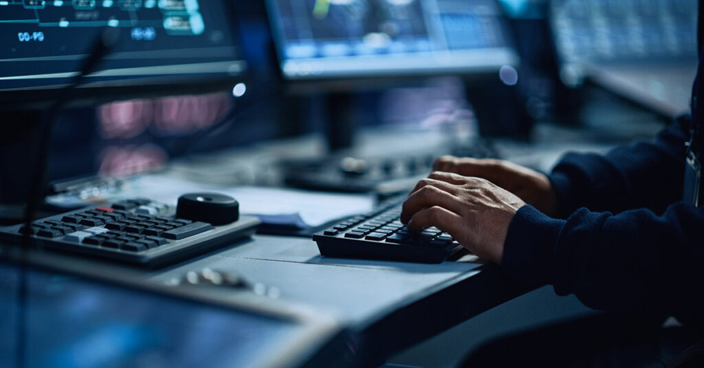 A person types on a keyboard in a security operations and surveillance center.