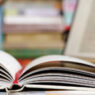 An open book on a desk with a laptop in the background.