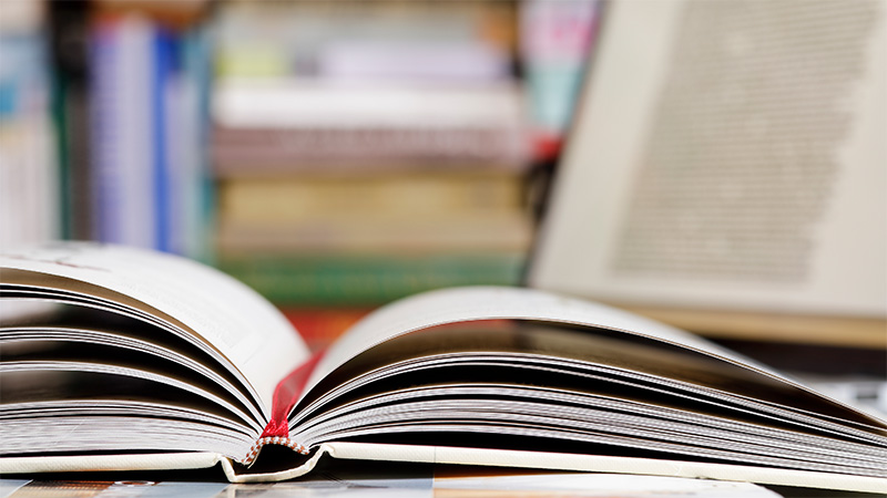 An open book on a desk with a laptop in the background.