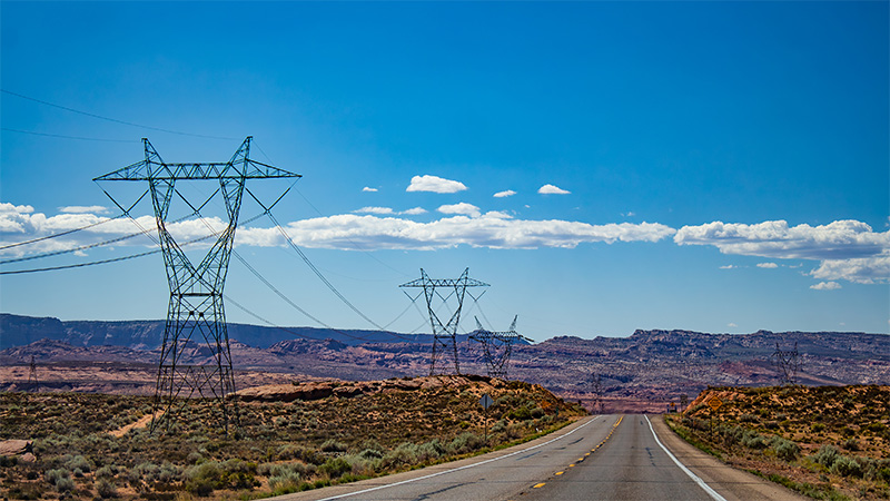 Power transmission pylpns standing alongside a road in the US Southwestern desert.