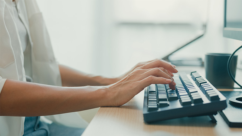 A person works at a desk, typing on a keyboard.