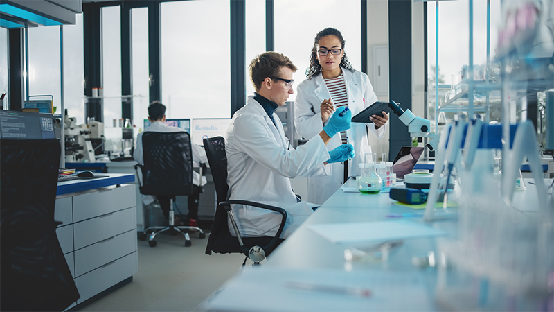 Two students work in a lab, reviewing data on a tablet.