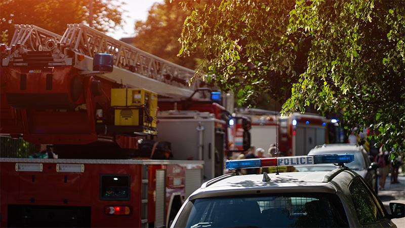 A fleet of fire trucks and police cruisers parked on a street.
