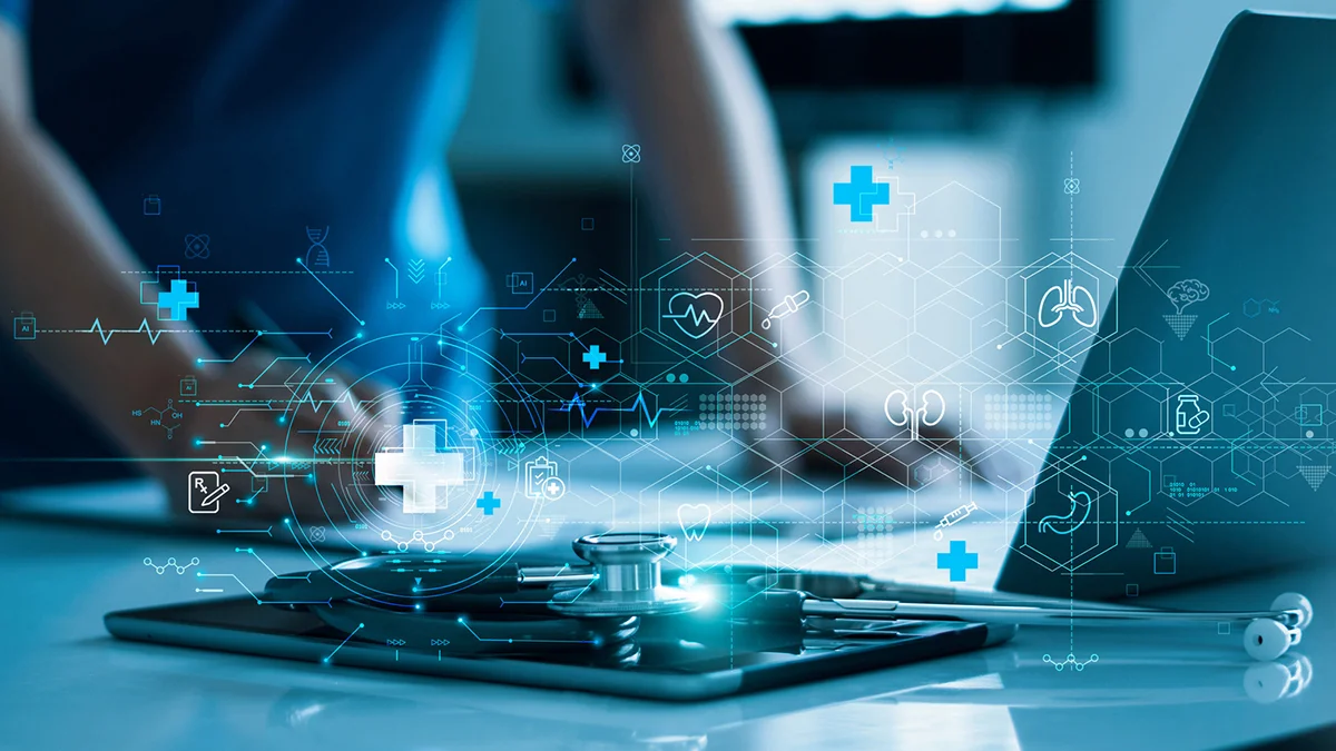 A healthcare professional works on a laptop and tablet, handling clinical duties and sensitive patient data.